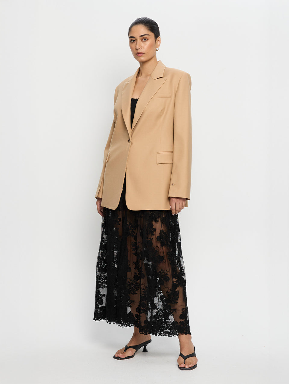 Woman wearing a beige blazer and black lace dress on a white background