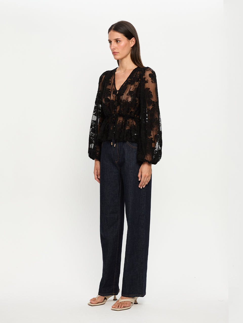 Woman wearing a black lace top and dark pants on a white background