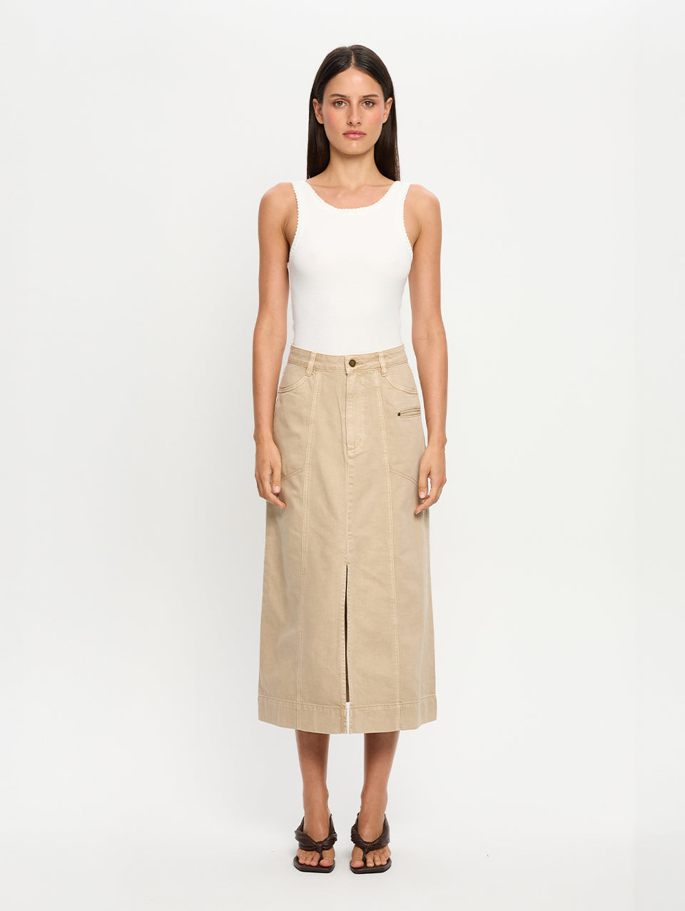 Woman wearing a white tank top and beige denim midi skirt on a white background