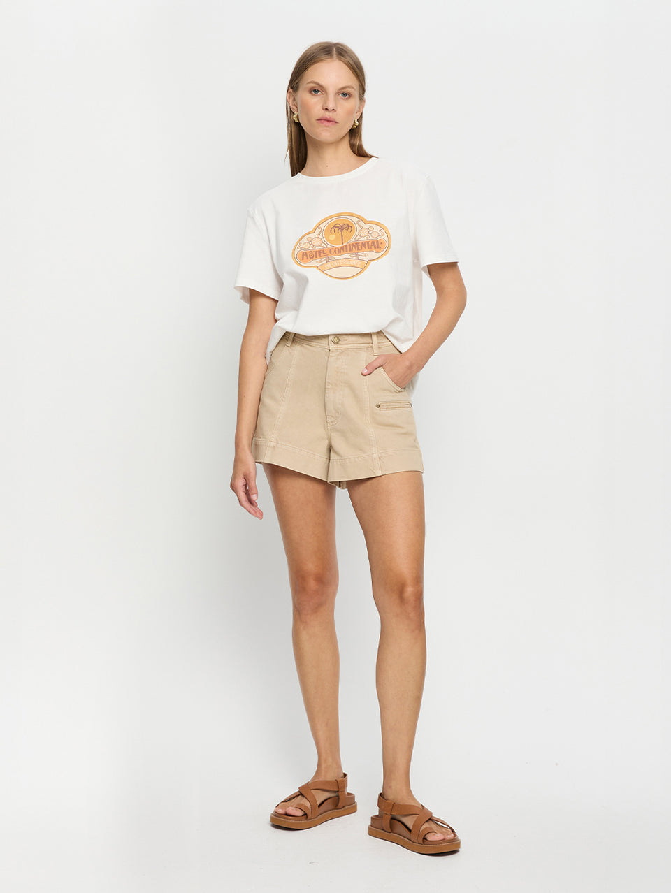 Woman wearing a white t-shirt with a logo and beige shorts on a white background