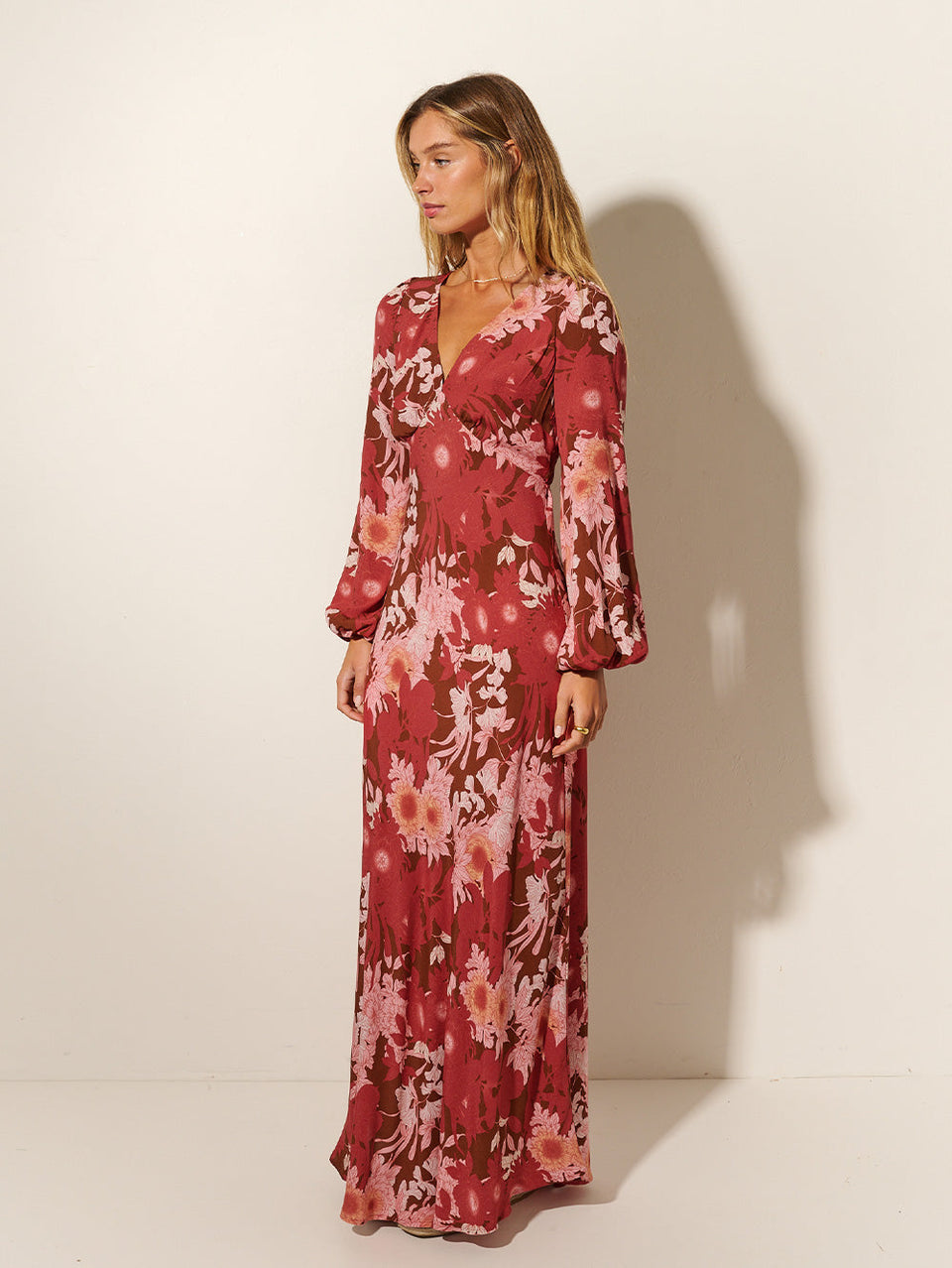 Studio model wears KIVARI Hacienda Tie Back Maxi Dress: A red, pink and brown floral dress crafted from sustainable LENZING Viscose Crepe in a bias cut with underbust seams, long sleeves and cut-out back with keyhole ties.