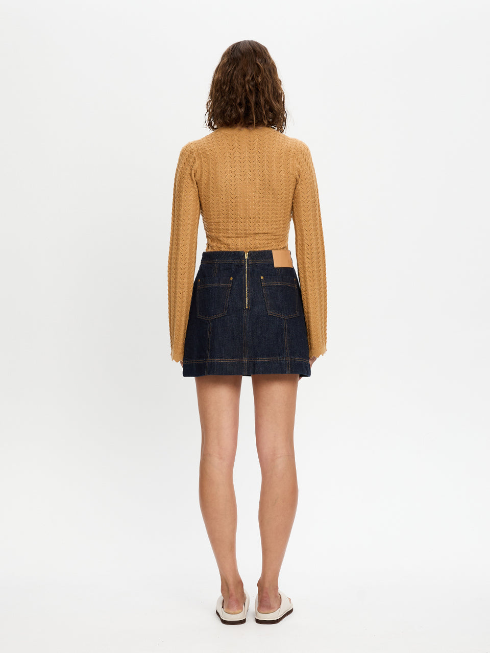 Woman wearing a mustard yellow checkered top and dark denim skirt on a white background