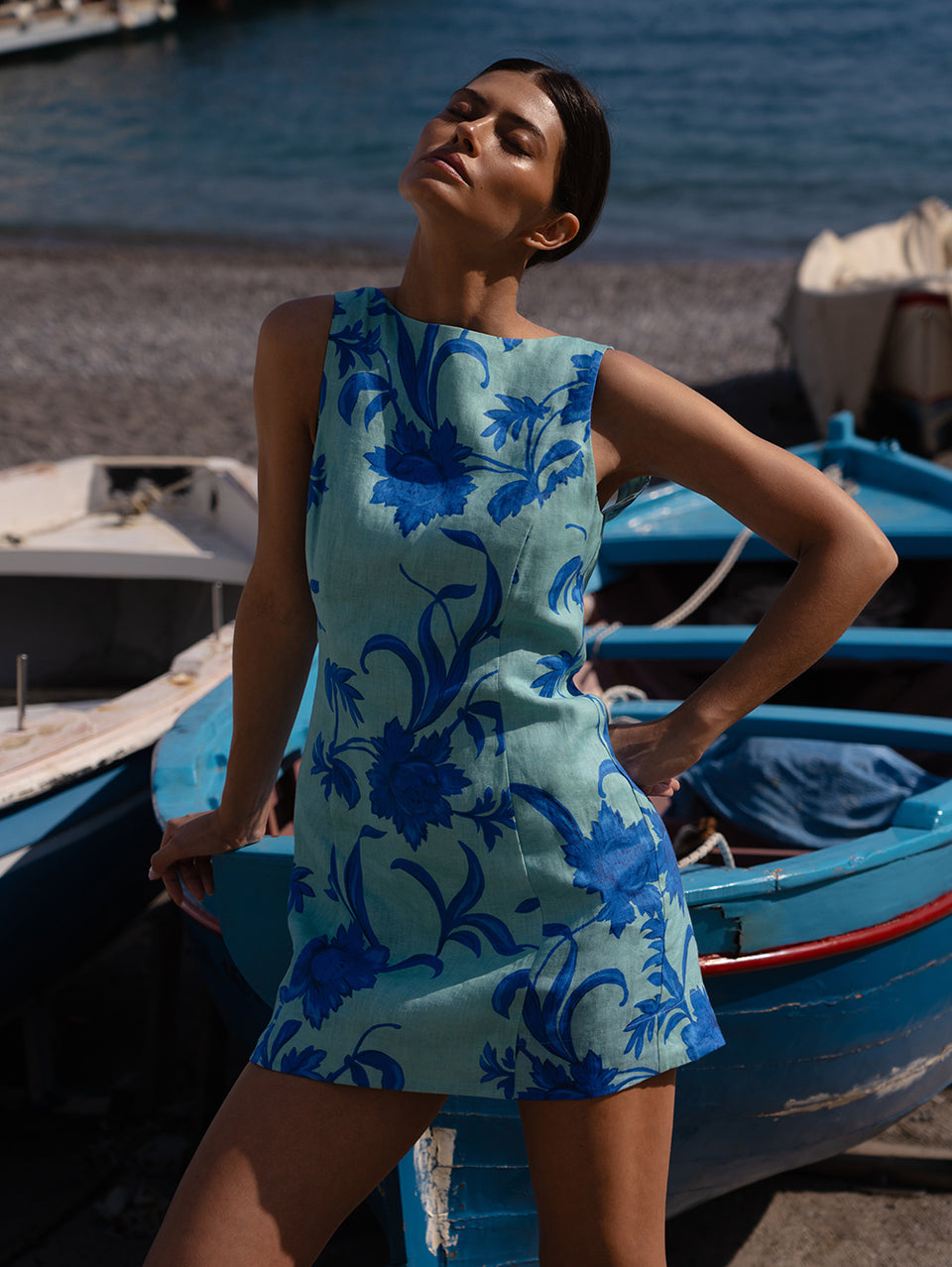Woman in a blue floral dress standing near boats by the water