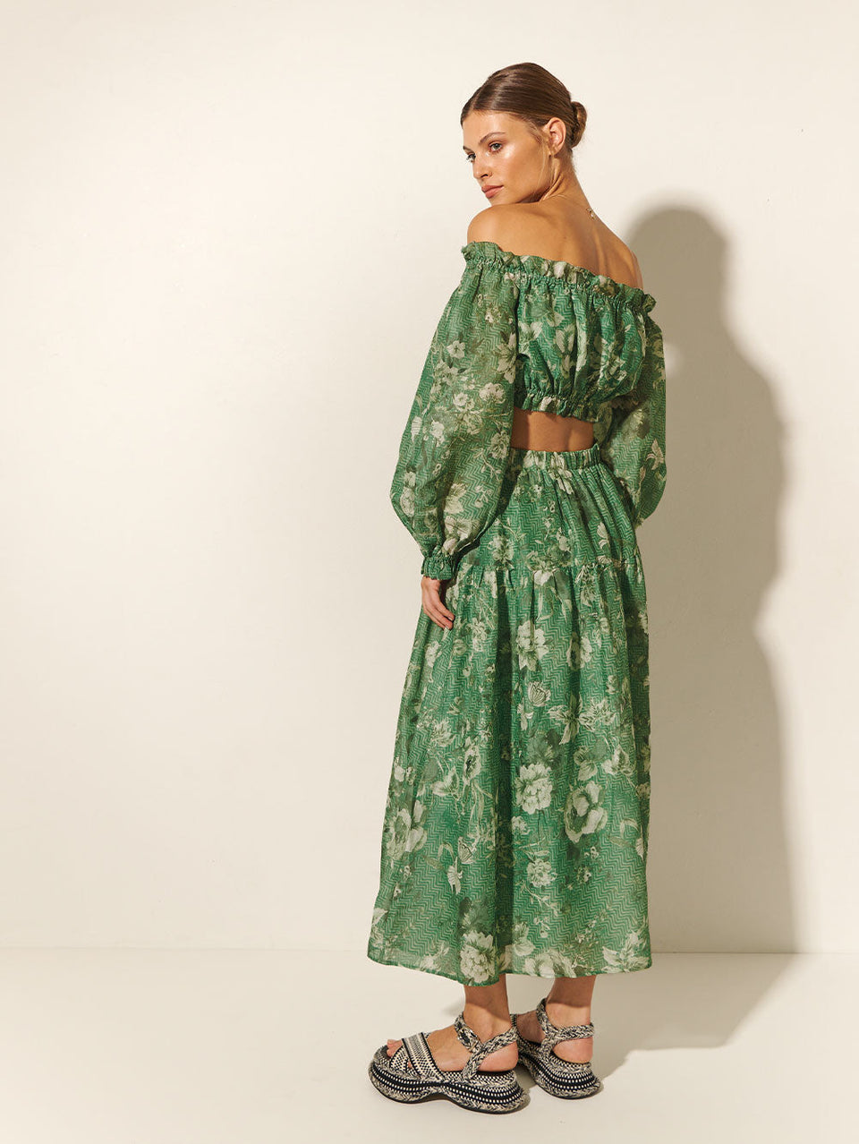 Studio model wears KIVARI Khalo Midi Skirt: A green floral midi skirt featuring an elasticated drawstring waist with gold bead ends and a gathered tiered skirt.