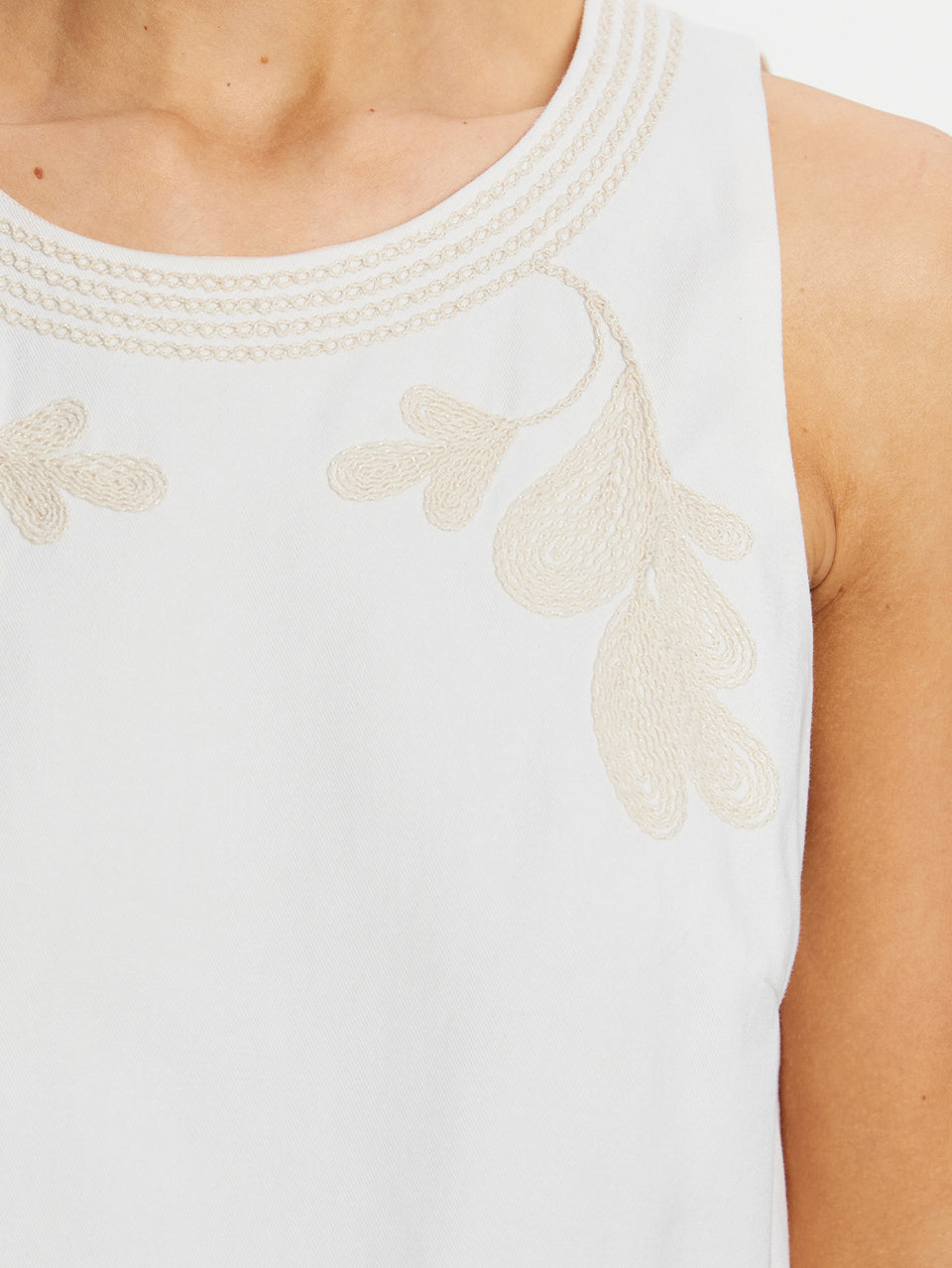 White sleeveless top with embroidery on a person wearing it.