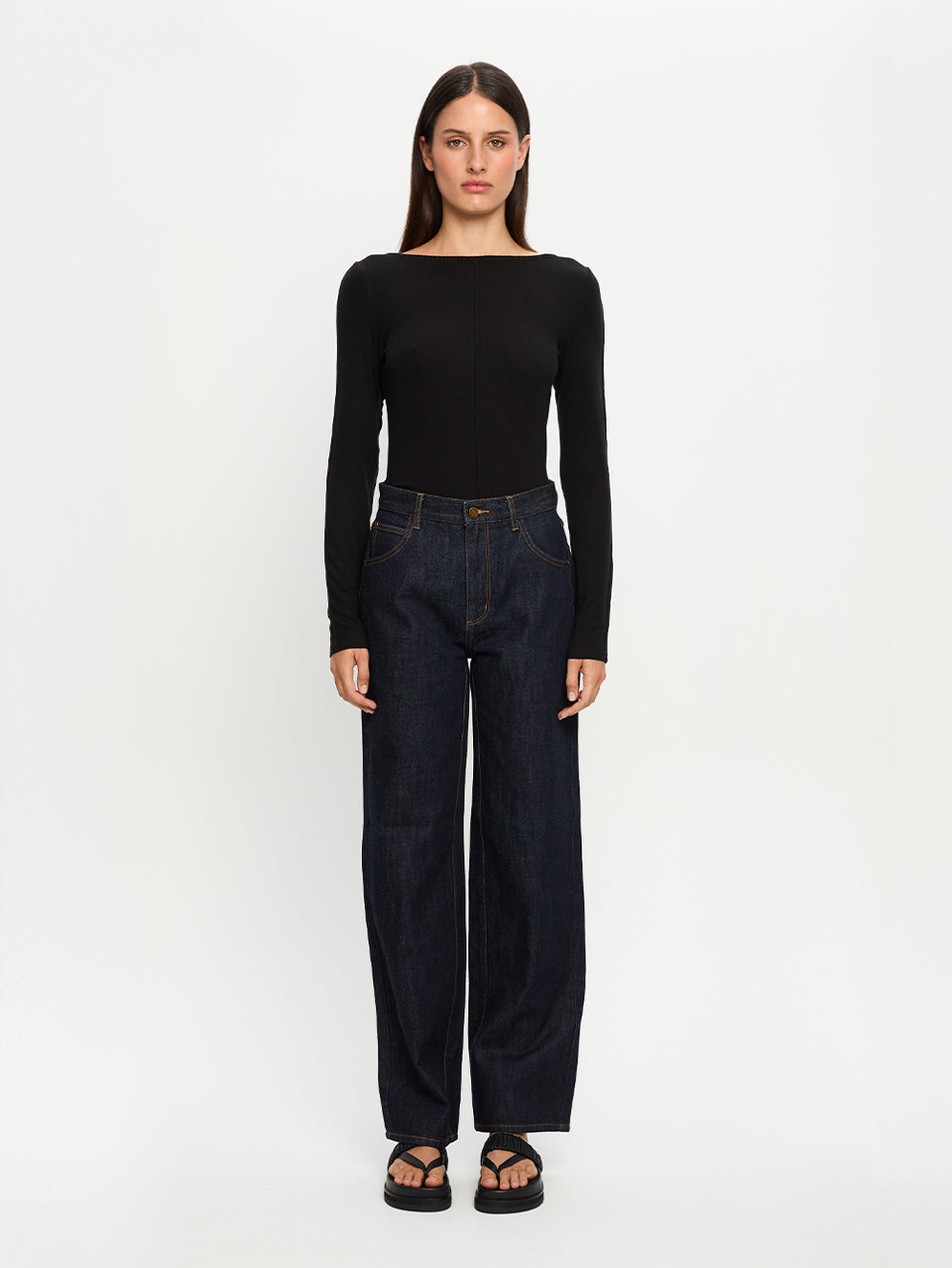 Woman wearing a black long-sleeve top and dark jeans on a white background