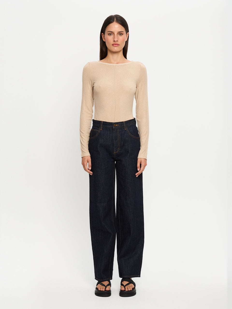 Woman wearing a beige top and black pants on a white background
