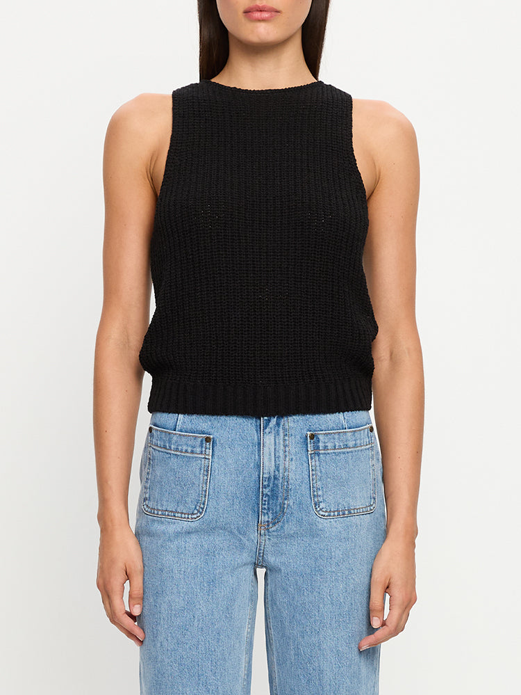 Person wearing a black sleeveless knit top and light blue jeans on a white background