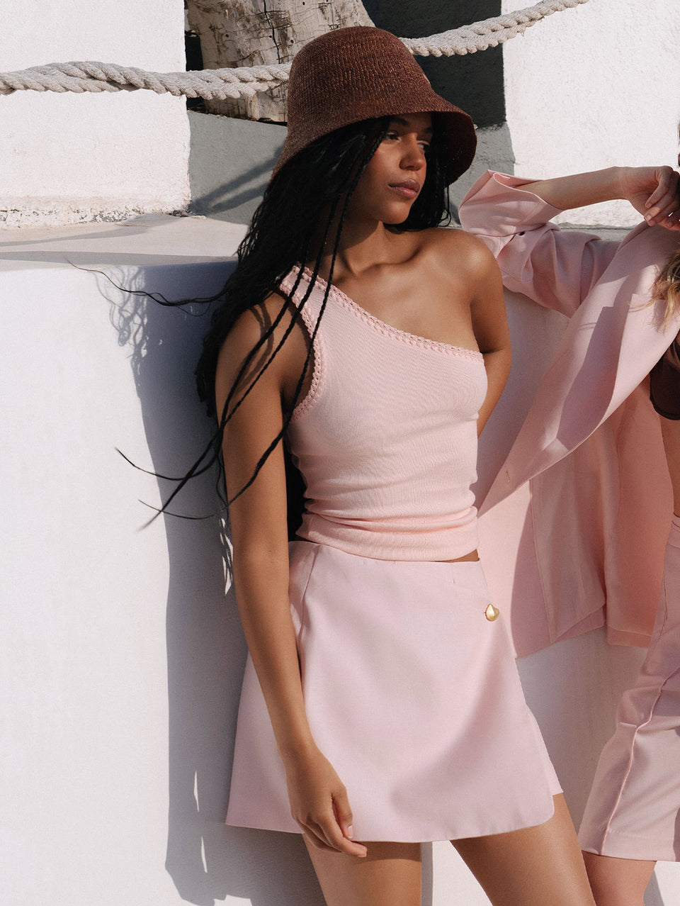 Woman wearing a pink outfit with a brown hat against a white wall.