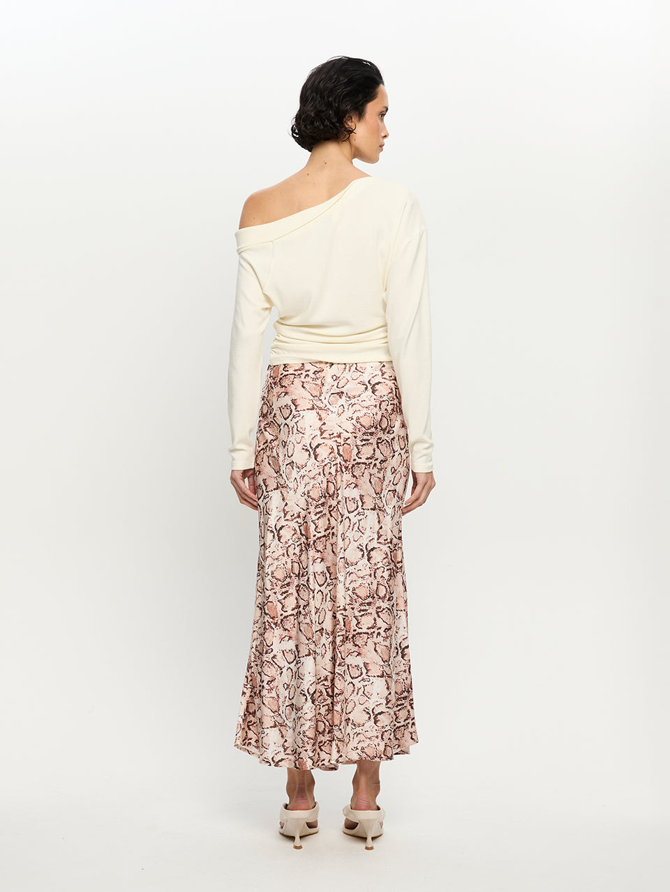 Woman wearing a white off-shoulder top and a patterned skirt on a white background