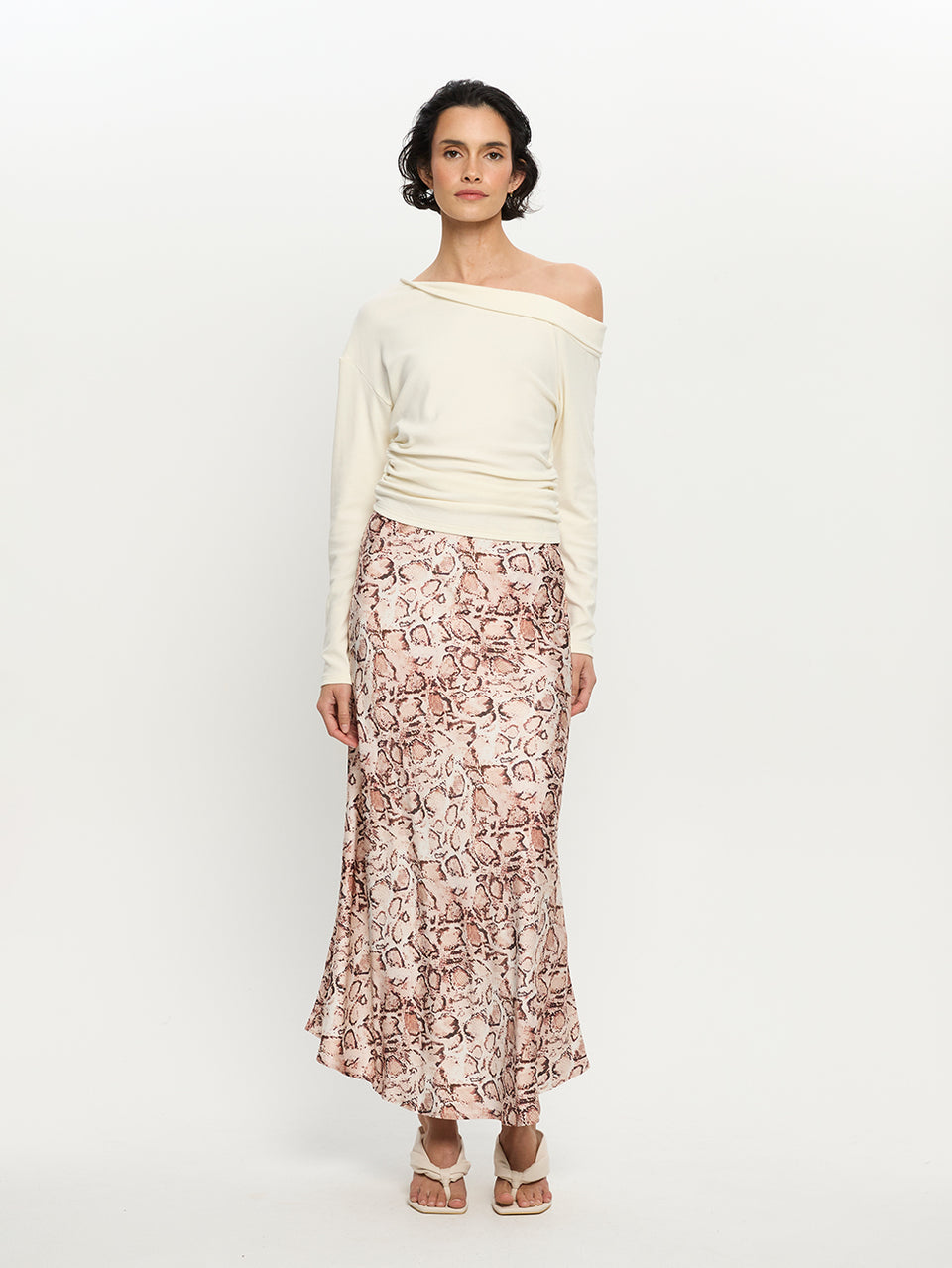 Woman wearing a white off-shoulder top and patterned skirt on a white background