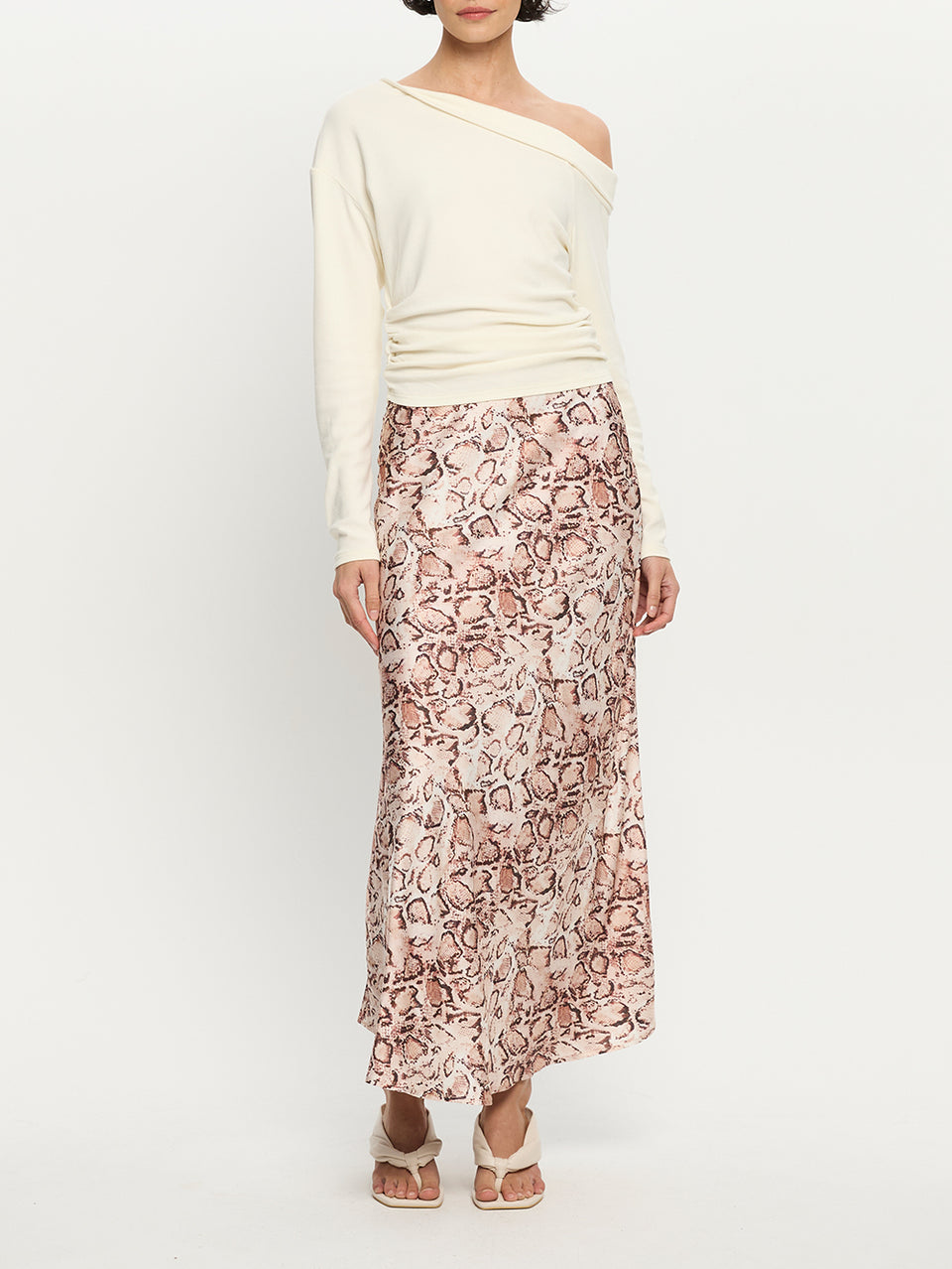 Woman wearing a white off-shoulder top and a long, patterned skirt on a white background