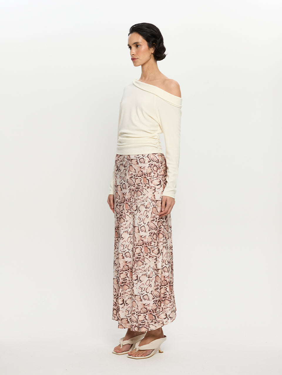 Woman wearing a white off-shoulder top and patterned skirt on a white background