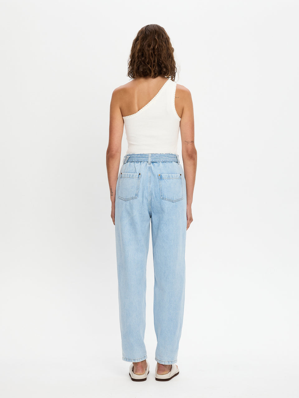 Woman wearing light blue jeans and a white one-shoulder top on a white background