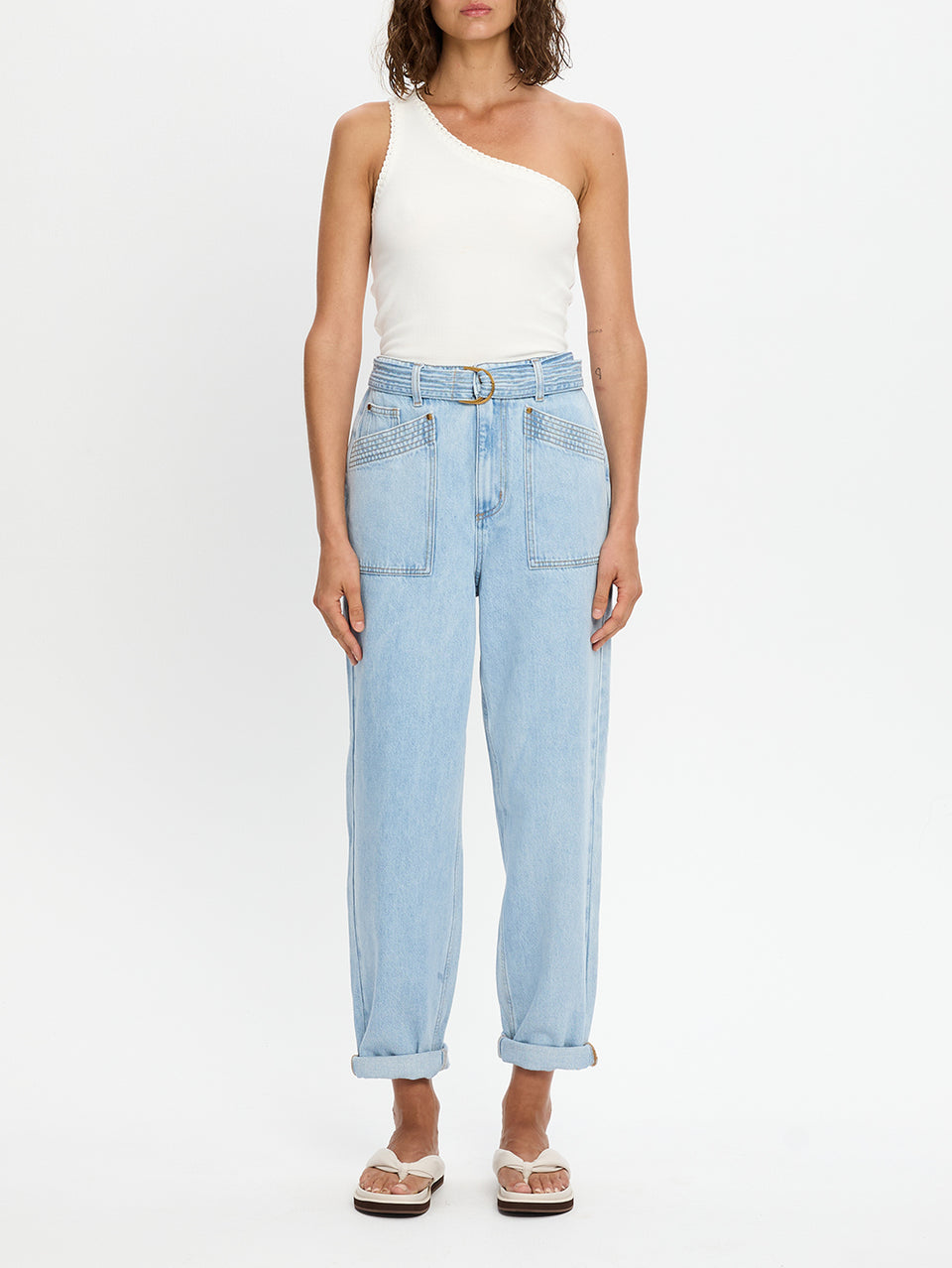Woman wearing light blue jeans and a white one-shoulder top on a white background