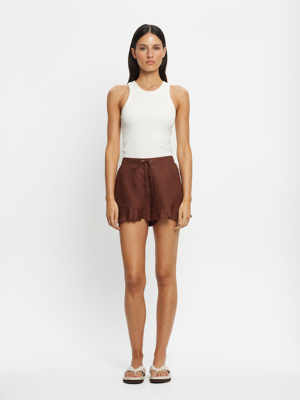 Woman wearing a white sleeveless top and brown shorts on a white background