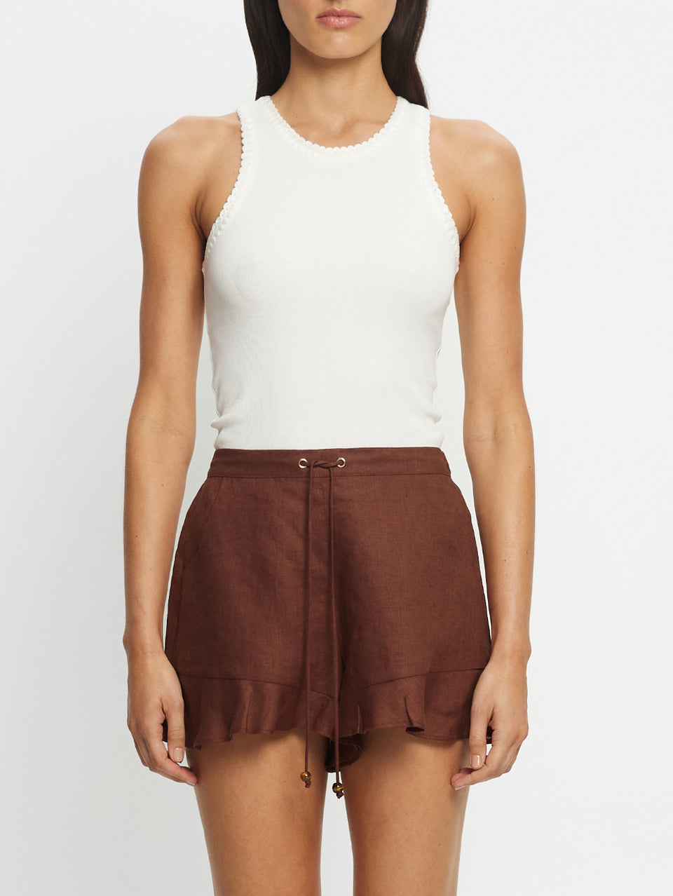 Woman wearing a white sleeveless top and brown shorts on a white background