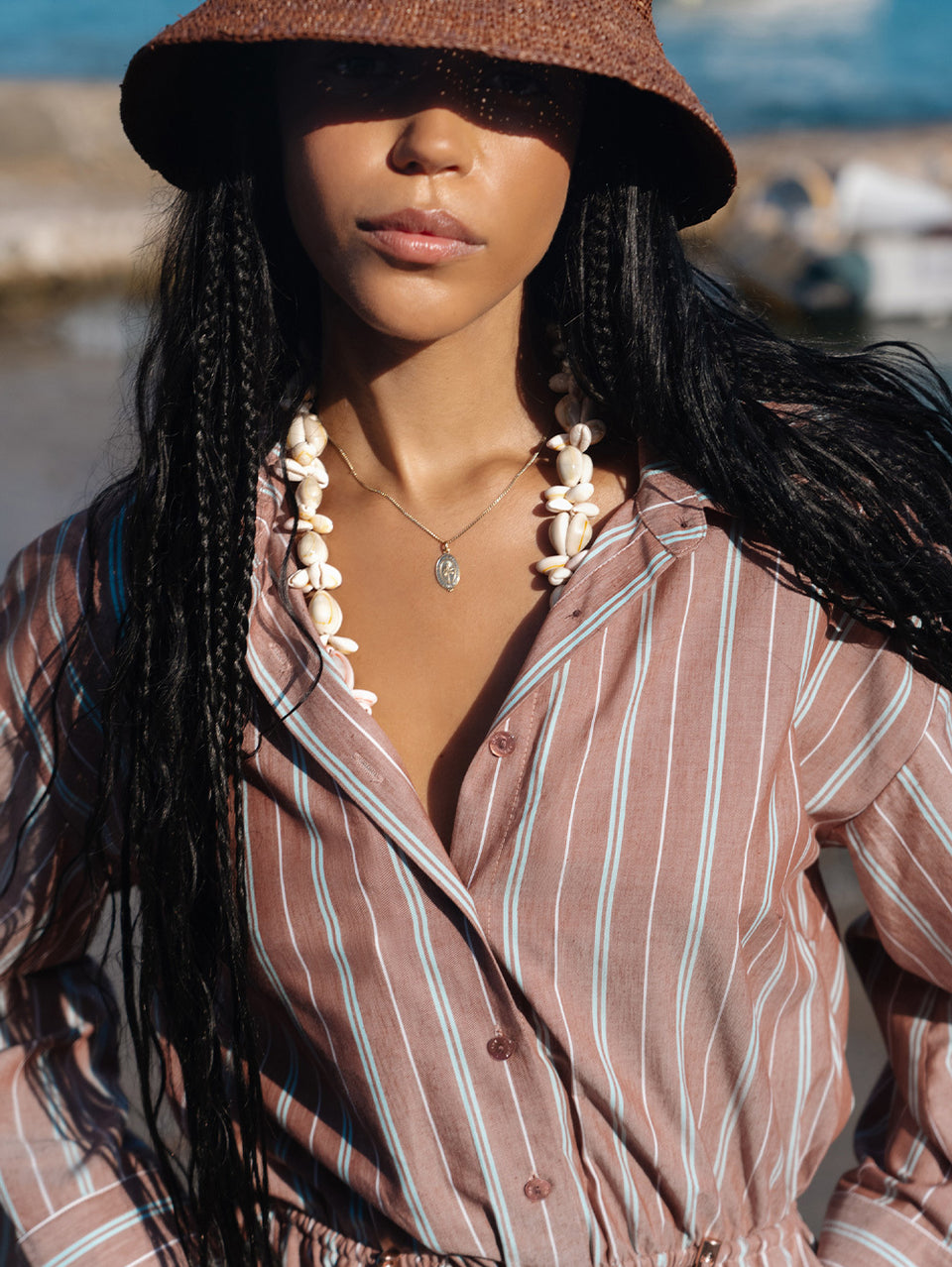 Woman wearing a brown hat and striped playsuitwith long braided hair, outdoors.