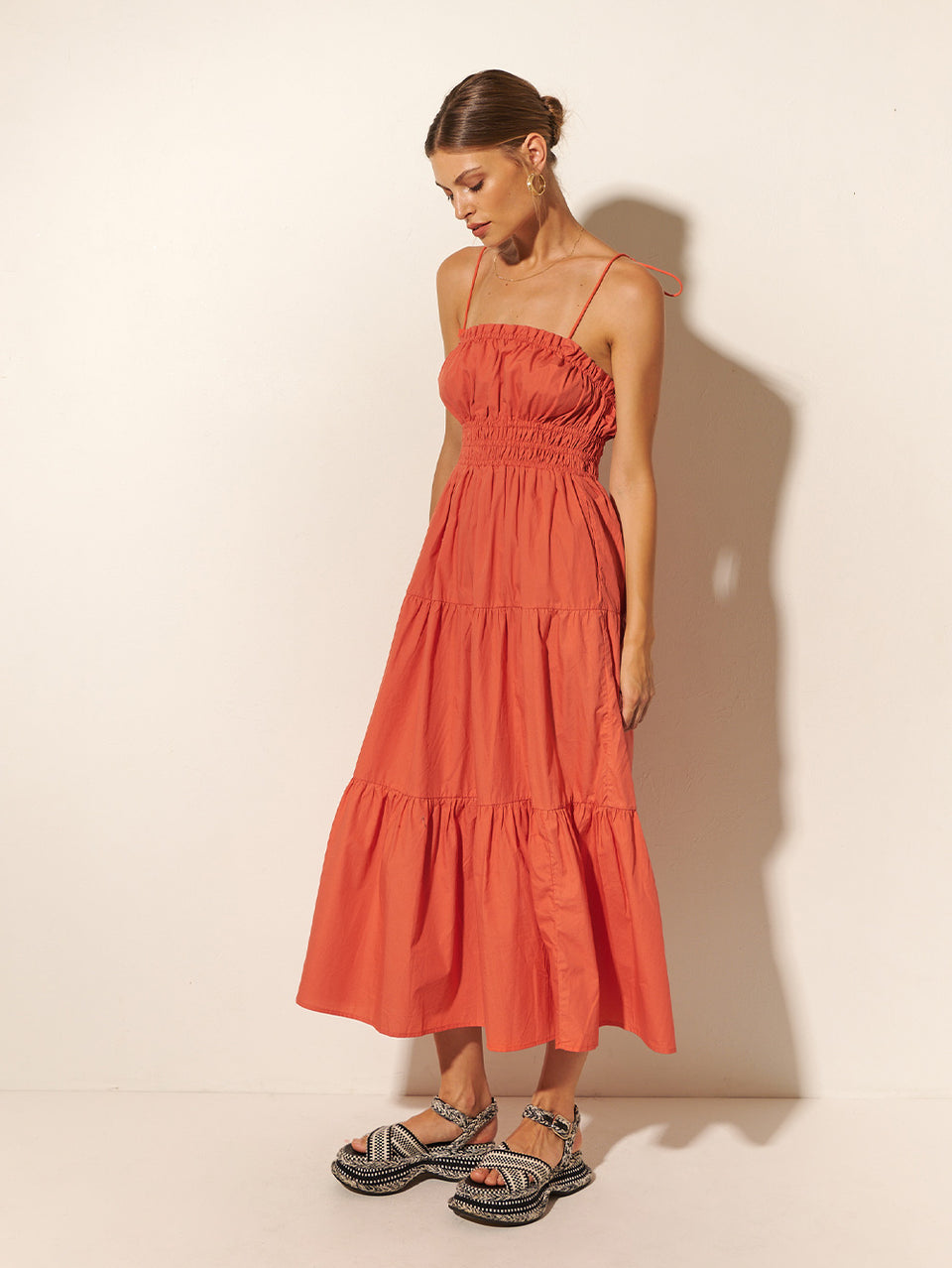 Studio model wears KIVARI Casini dress - a coral block colour dress with thin straps, elasticated waist and tiered skirt.