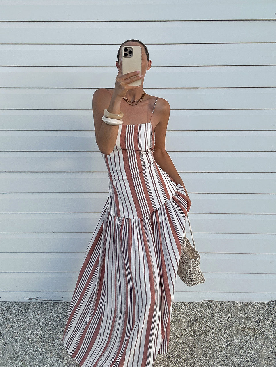 Woman wearing a striped dress against a white wall.