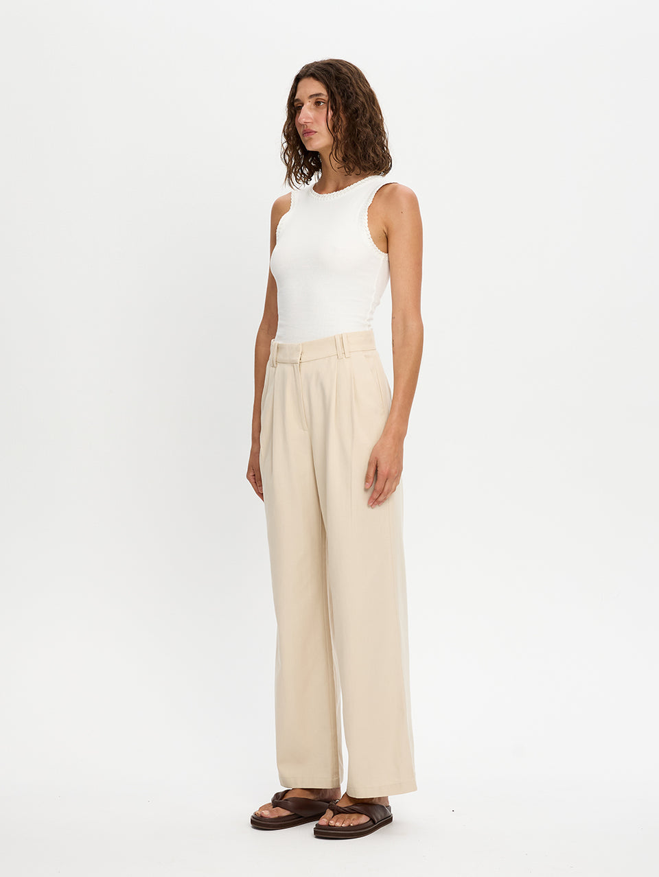 Woman wearing a white sleeveless top and beige pants on a white background