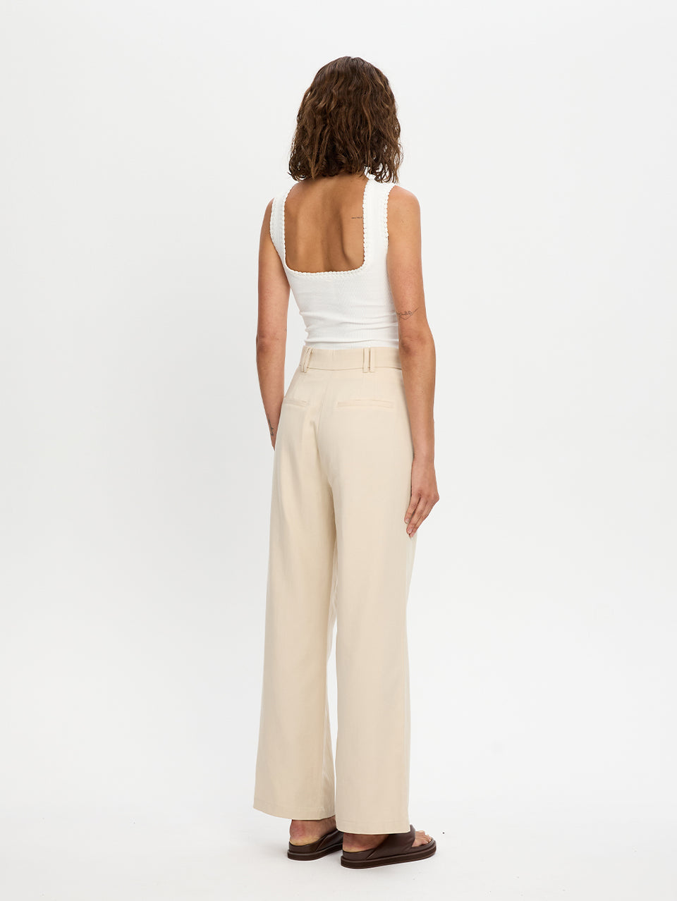 Woman wearing a white sleeveless top and beige wide-leg pants on a white background