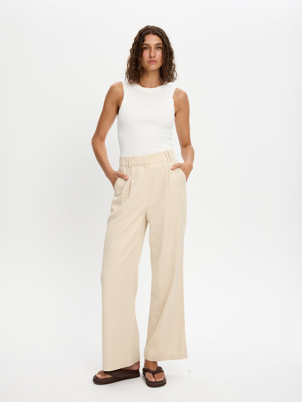 Woman wearing a white sleeveless top and beige wide-leg pants on a white background