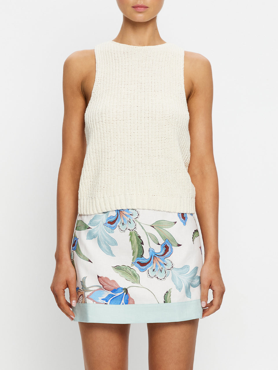 Woman wearing a cream sleeveless top and floral skirt on a white background