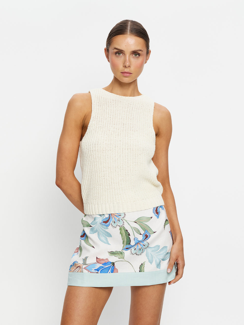 Woman wearing a cream sleeveless top and floral skirt on a white background