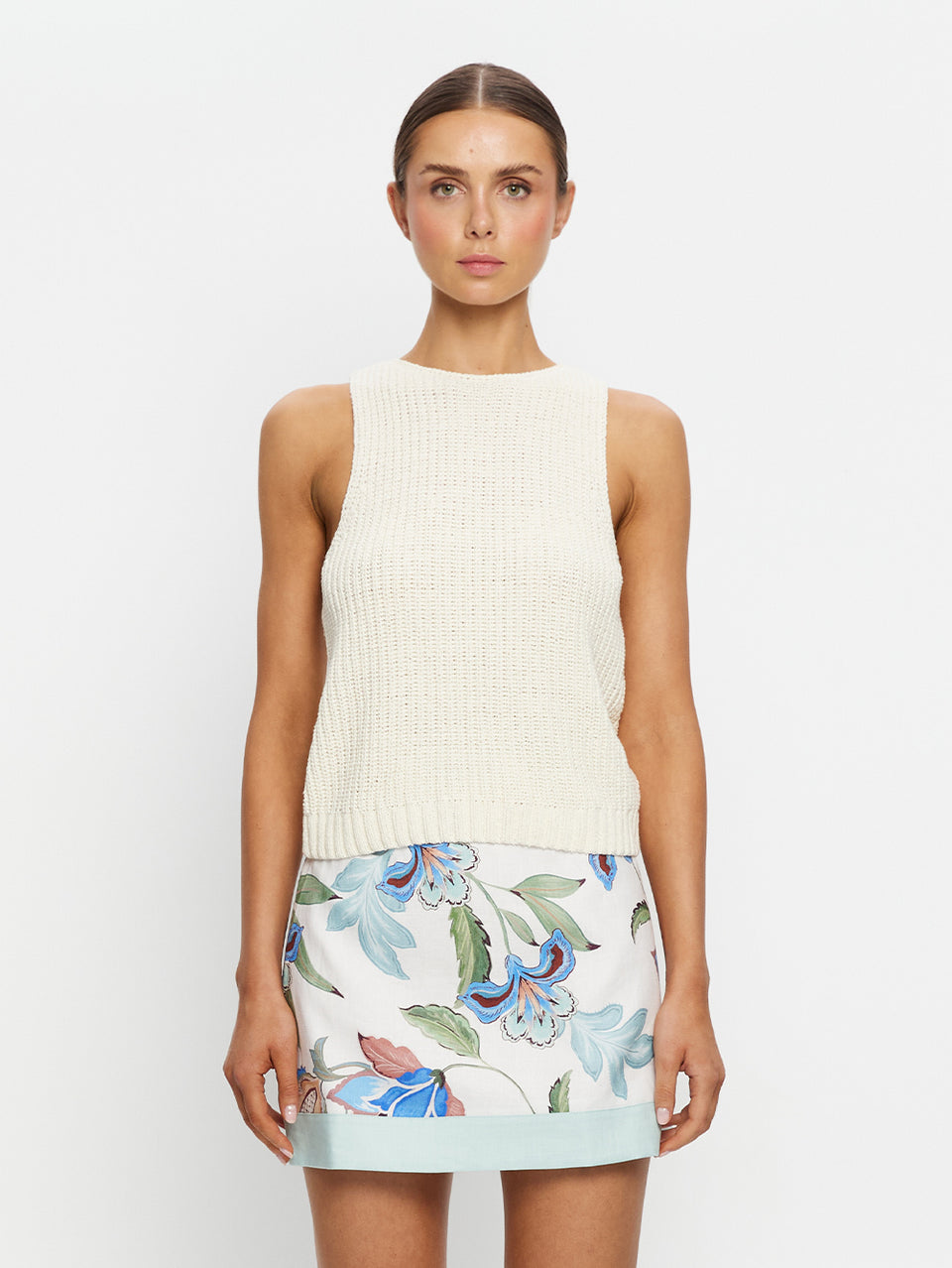 Woman wearing a white sleeveless top and floral skirt on a plain background