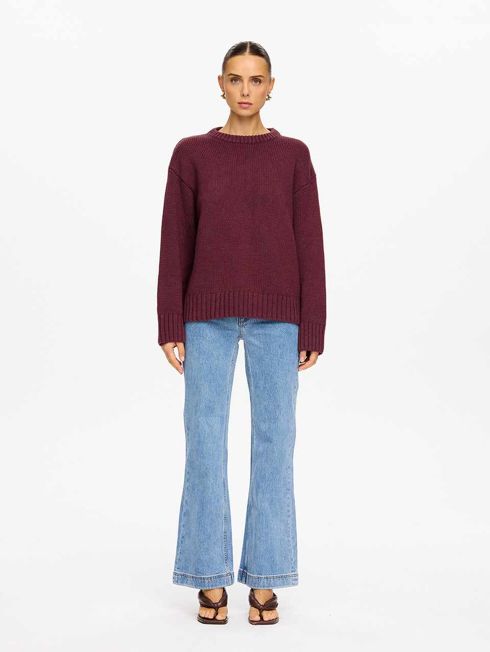 KIVARI Odette Crew Neck Jumper in Plum - front view of model wearing dark burgundy ribbed crew neck knit jumper with light blue flared jeans