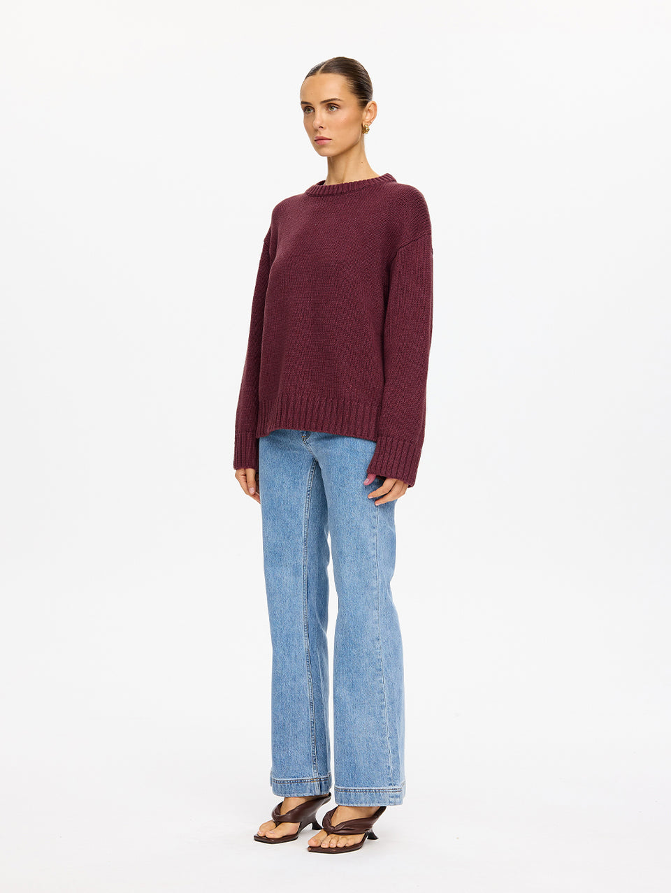 KIVARI Odette Crew Neck Jumper in Plum – full-length front view of model wearing women's dark burgundy ribbed knit crew neck jumper with blue jeans on white background