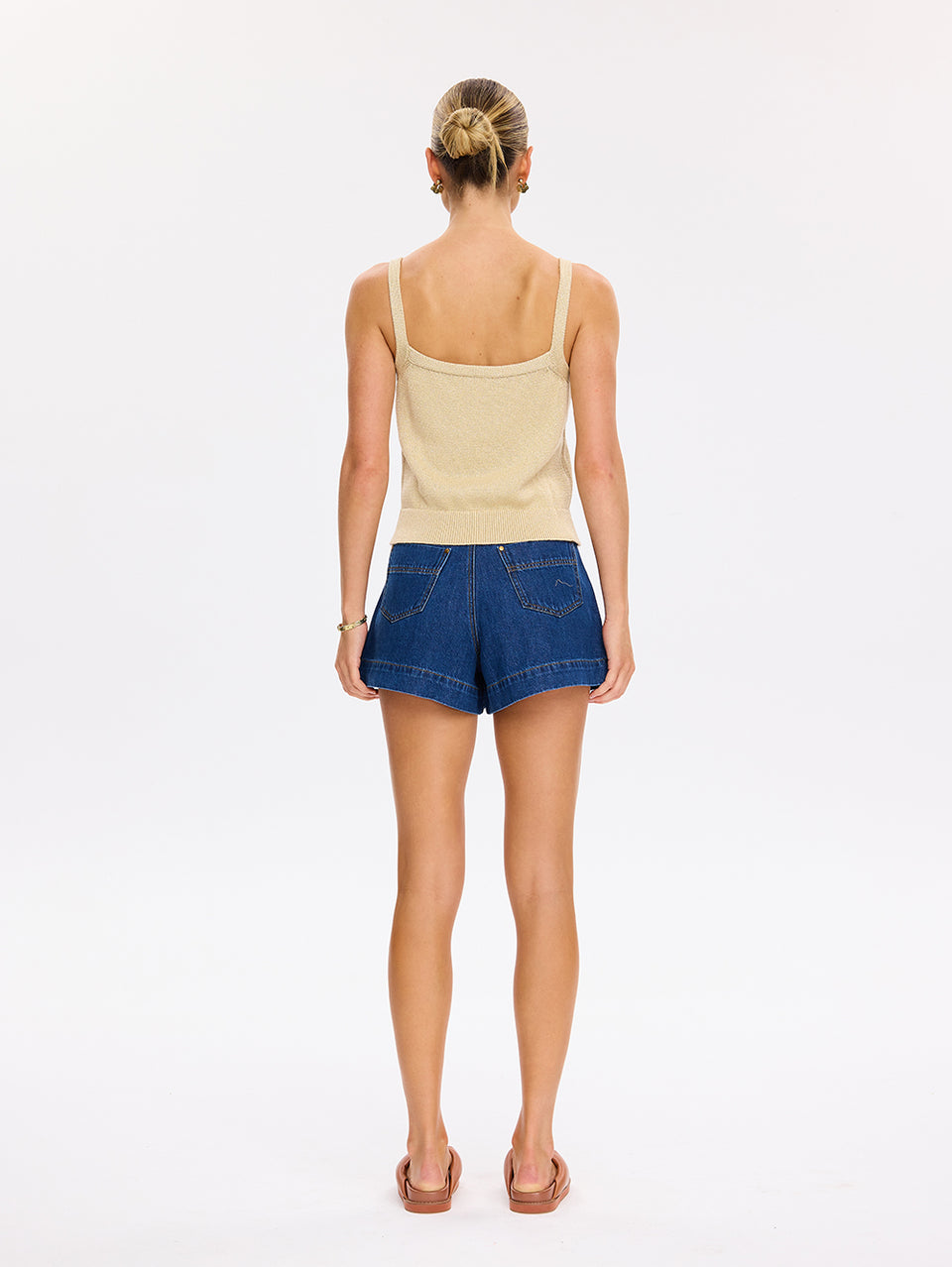 Woman wearing a beige tank top and blue denim shorts on a white background