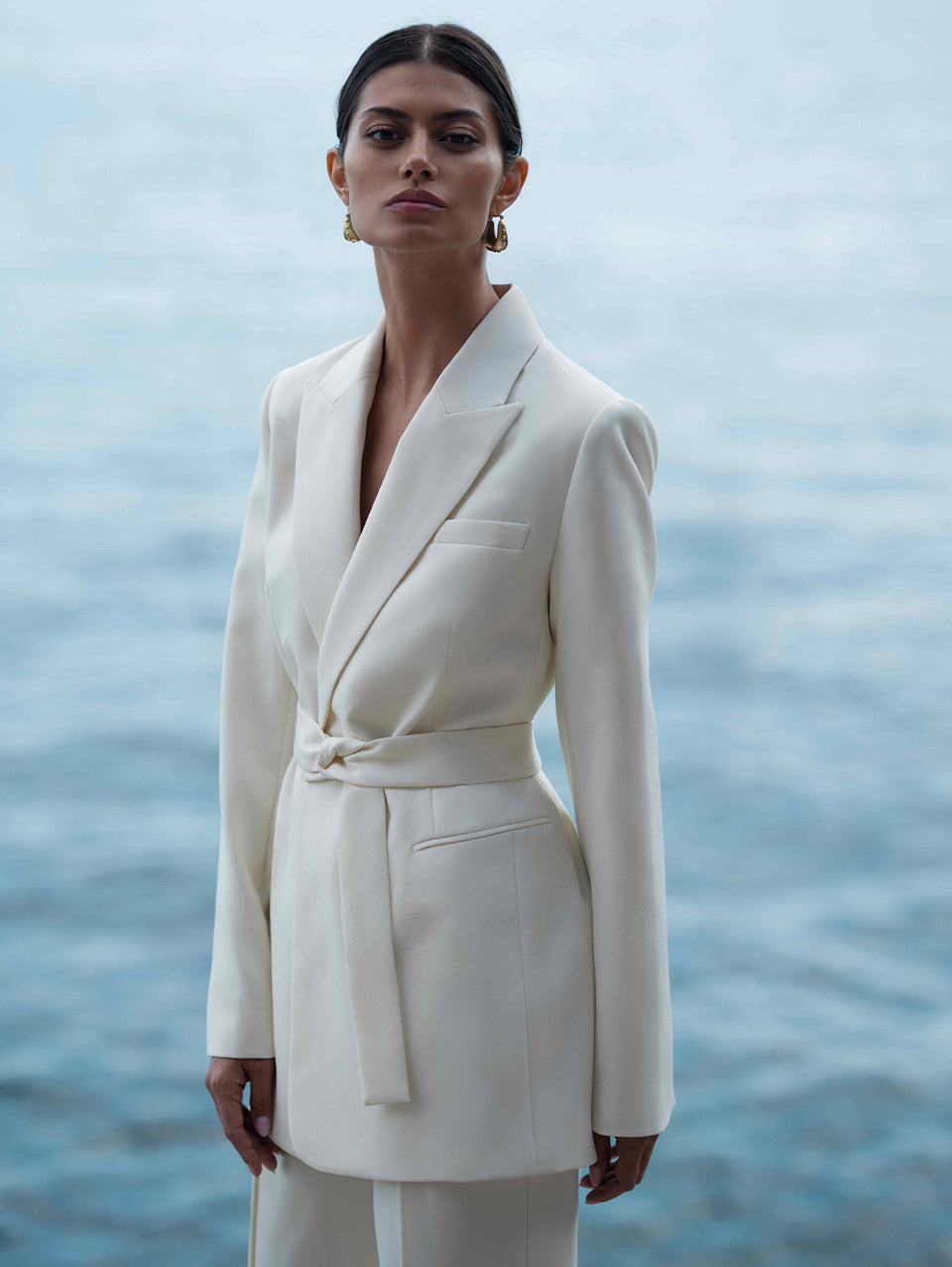 Woman wearing a white suit standing against a blue water background