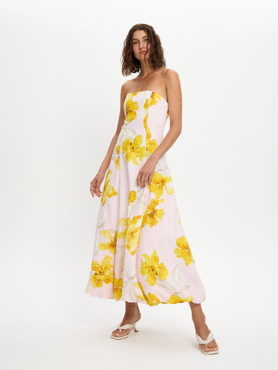 Woman wearing a strapless dress with yellow floral pattern on a white background