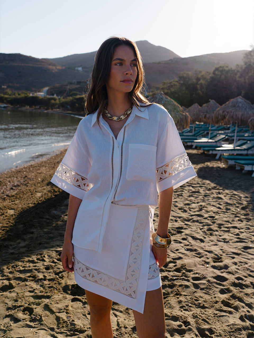 Woman in a white dress with lace details standing on a beach.