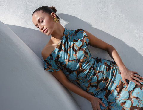 KIVARI editorial lifestyle shot - model reclining against white stone wall wearing blue and brown floral dress