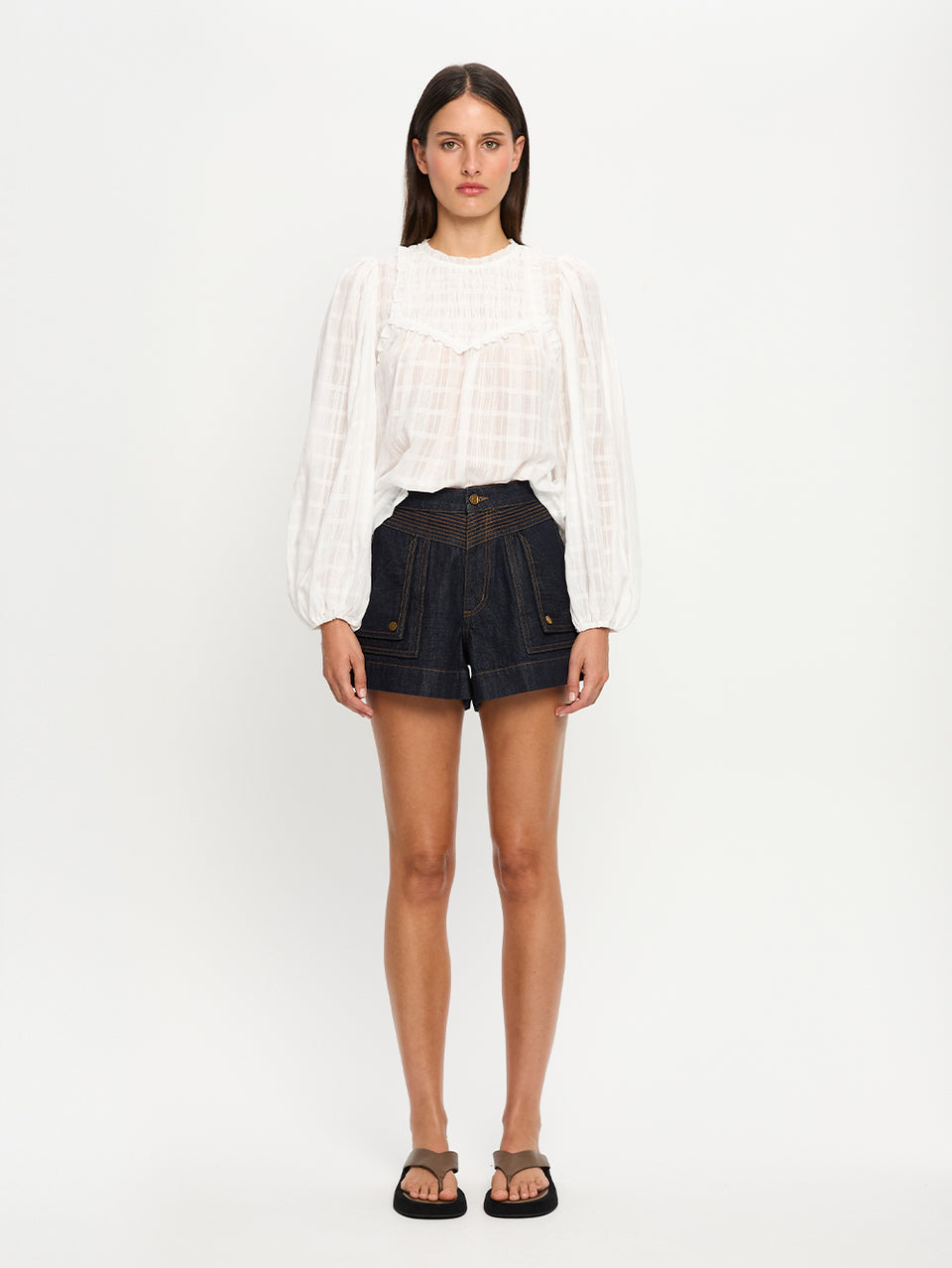Woman wearing a white blouse and dark denim shorts on a white background