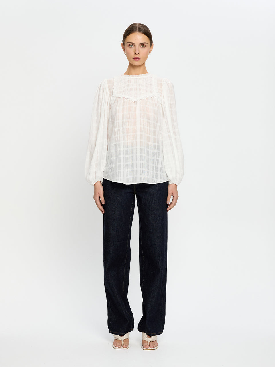 Woman wearing a white blouse and navy jeans on a white background