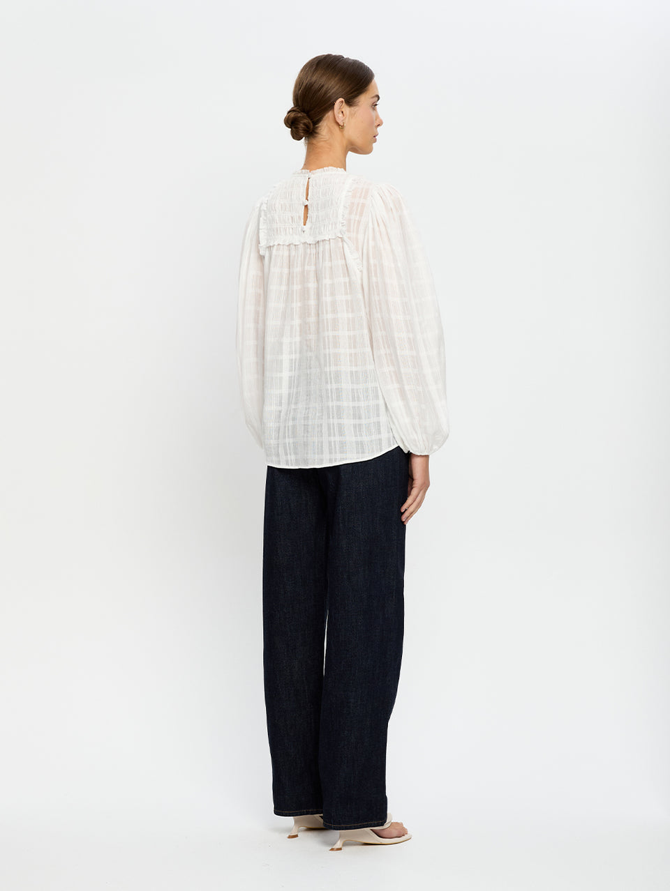 Woman wearing a white blouse and navy jeans on a white background