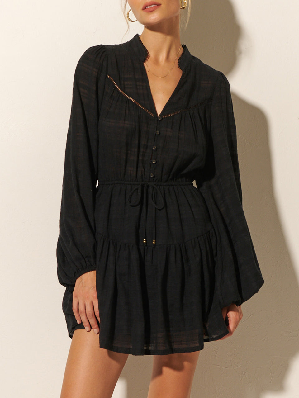 Close up: Studio model wears the KIVARI Rafaelle Mini Dress: a black dress made from cotton check featuring a button-front bodice, full-length blouson sleeves, drawstring waist and gathered hem frill.