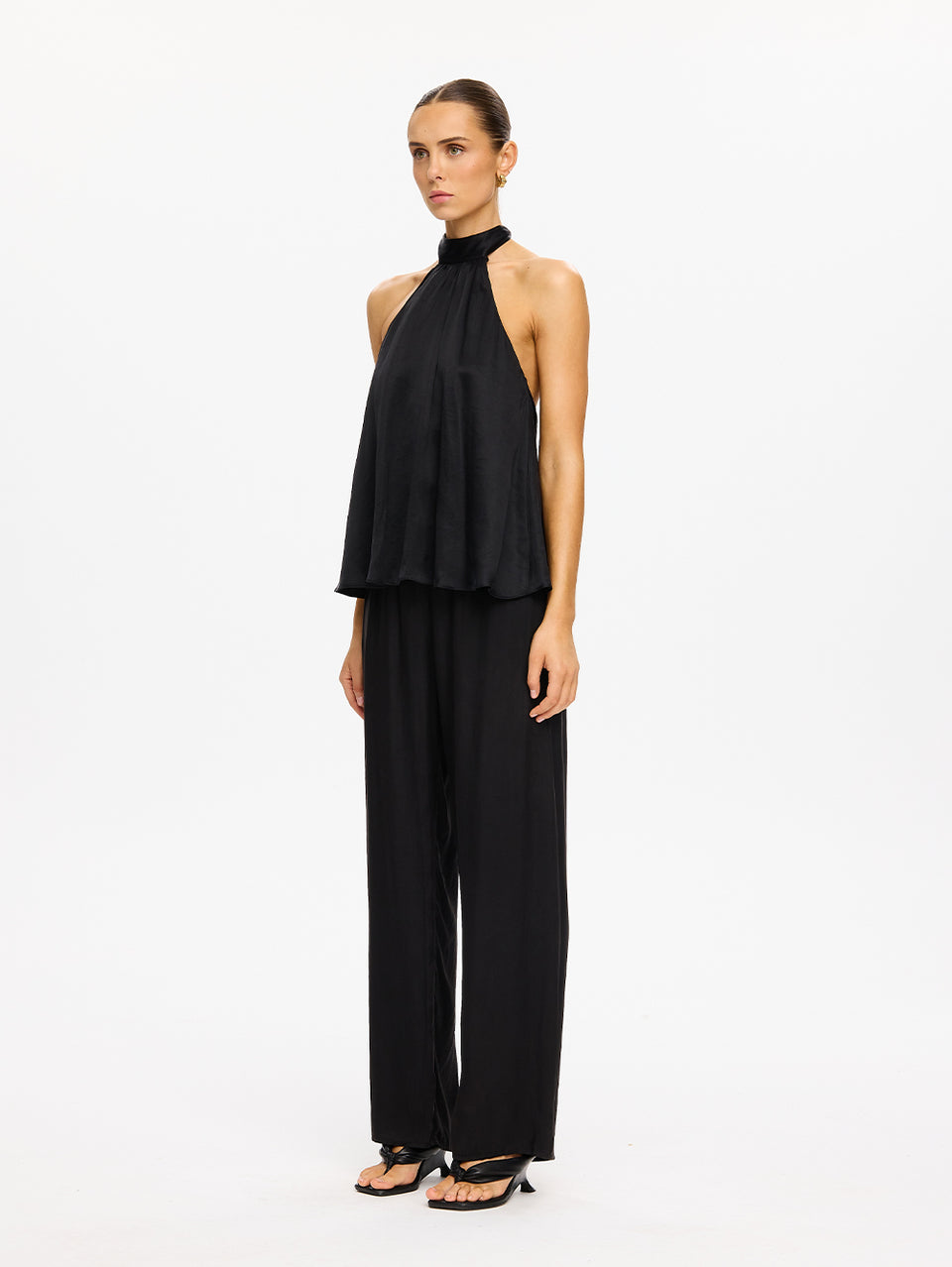 KIVARI Jaxon Halter Top in Black – full-length side view of model wearing women's black halter neck top with wide-leg pants and strappy heels