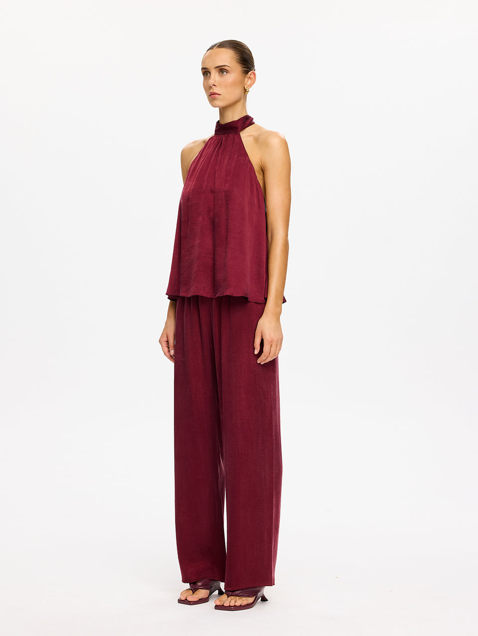 KIVARI Jaxon Halter Top in Plum – full-length side view of model wearing women's plum halter neck top with matching wide-leg pants and heels