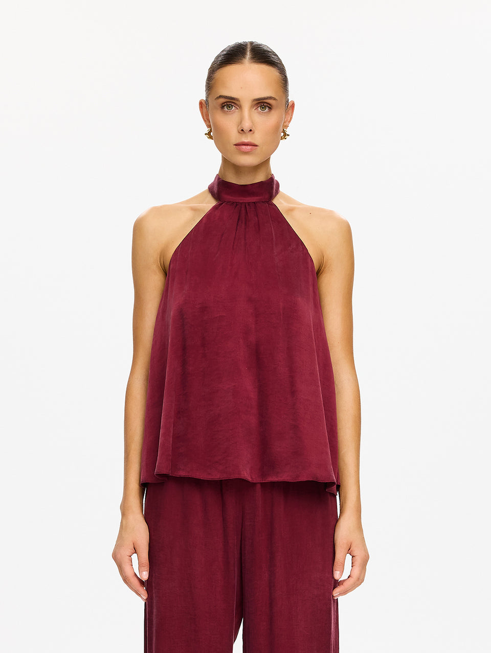 KIVARI Jaxon Halter Top in Plum – model wearing women's plum halter neck top with wide-leg pants, gold earring detail